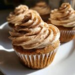 Close-up of a moist pumpkin spice latte cupcake topped with creamy frosting and a sprinkle of cinnamon.