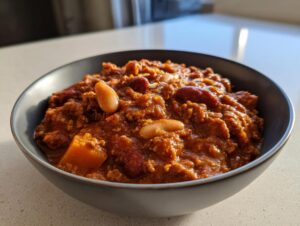 A close-up of a bowl filled with hearty pumpkin turkey chili, featuring kidney beans, white beans, and chunks of pumpkin.
