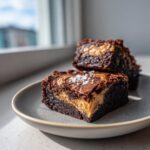 Two rich, dark chocolate brownies with a gooey salted caramel filling, topped with sea salt flakes.