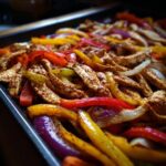 Close-up of colorful sliced bell peppers and seasoned chicken strips on a baking sheet for sheet pan chicken fajitas.