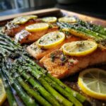 Close-up of perfectly cooked sheet pan salmon and asparagus topped with lemon slices and herbs.