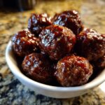 Close-up of a white bowl filled with glistening slow cooker BBQ meatballs.