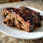 Close-up of tender, juicy slow cooker beef brisket slices with a glossy glaze on a white plate.