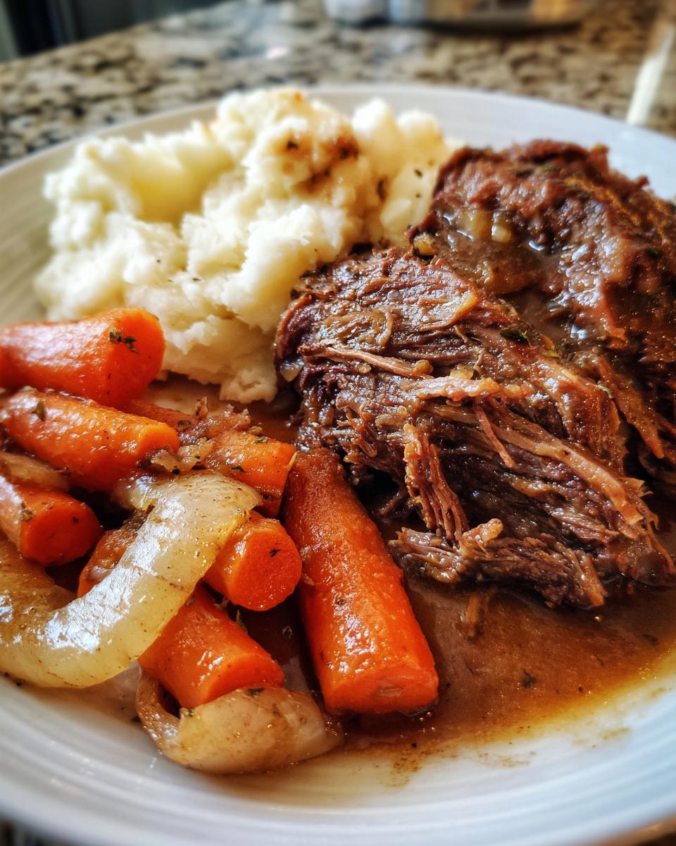 A close-up of a plate of slow cooker pot roast served with mashed potatoes and tender carrots and onions.