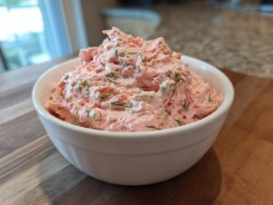A close-up of a white bowl filled with creamy smoked salmon dip, garnished with fresh dill.