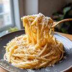 A fork lifting a generous portion of Spaghetti Carbonara, topped with grated Parmesan cheese and black pepper.