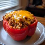 A close-up of a red stuffed bell pepper filled with seasoned ground beef and rice, topped with melted cheddar cheese.