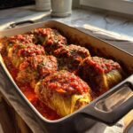 A baking dish filled with tender stuffed cabbage rolls, generously topped with a rich tomato sauce and sprinkled with fresh parsley.
