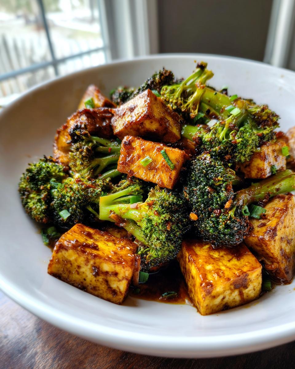 Close-up of a bowl filled with glistening tofu broccoli stir fry, featuring pan-fried tofu cubes and tender broccoli florets coated in a savory sauce.