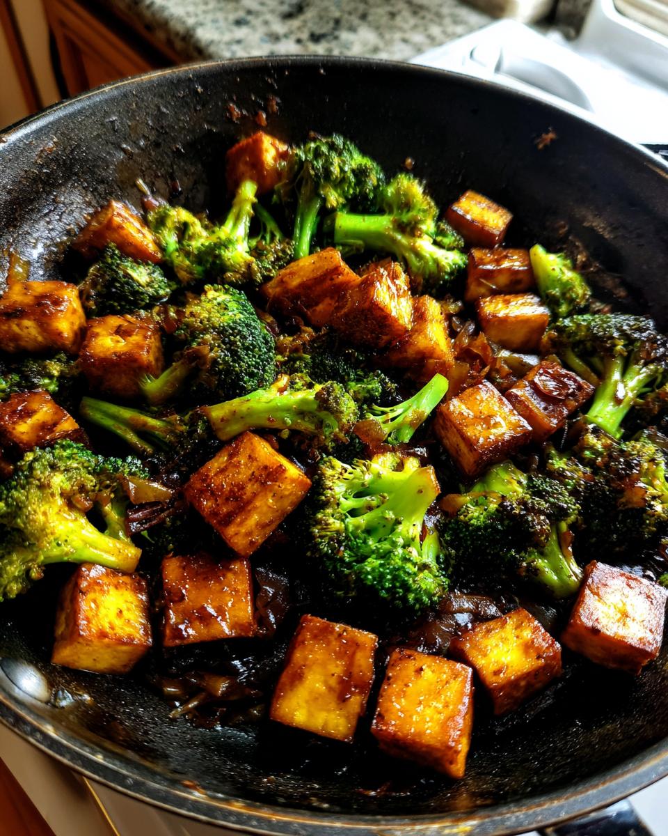 Close-up of a pan filled with a delicious tofu broccoli stir fry, featuring golden-brown tofu cubes and vibrant green broccoli florets coated in sauce.