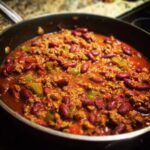 Close-up of a delicious vegetarian chili simmering in a skillet, featuring kidney beans, ground meat substitute, and chopped peppers.