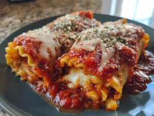 Close-up of two vegetarian lasagna rolls smothered in marinara sauce and topped with melted cheese and herbs.