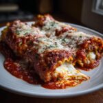 Close-up of three vegetarian lasagna rolls covered in marinara sauce and melted cheese, garnished with parsley.