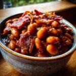 Close-up of a rustic bowl filled with savory baked beans, topped with crispy bacon and onions.