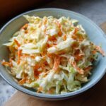 Close-up of a bowl of delicious coleslaw, featuring shredded cabbage and carrots mixed with a creamy dressing.