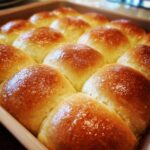 Close-up of freshly baked, golden brown dinner rolls in a baking pan, glistening with butter.
