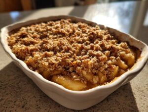 Close-up of a freshly baked apple crisp in a white baking dish, with a golden brown crumble topping.