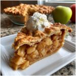A close-up of a generous slice of homemade apple pie, topped with a scoop of vanilla ice cream.