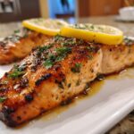 Close-up of two perfectly baked salmon fillets, glazed and topped with fresh parsley and lemon slices.