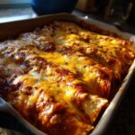 A close-up of freshly baked beef enchiladas covered in melted cheese and red sauce in a baking dish.