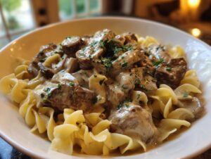A close-up of a white bowl filled with creamy Beef Stroganoff served over wide egg noodles, garnished with fresh parsley.