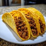 Three crispy shell beef tacos filled with seasoned ground beef and topped with shredded cheddar cheese.
