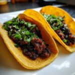 Close-up of two flavorful black bean tacos, generously filled and topped with fresh cilantro and diced onions.