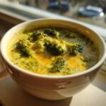 Close-up of a steaming bowl of creamy Broccoli Cheddar Soup with visible broccoli florets and melted cheddar cheese.