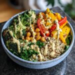 A vibrant and healthy Buddha bowl filled with quinoa, broccoli, chickpeas, bell peppers, and kale, drizzled with tahini dressing.