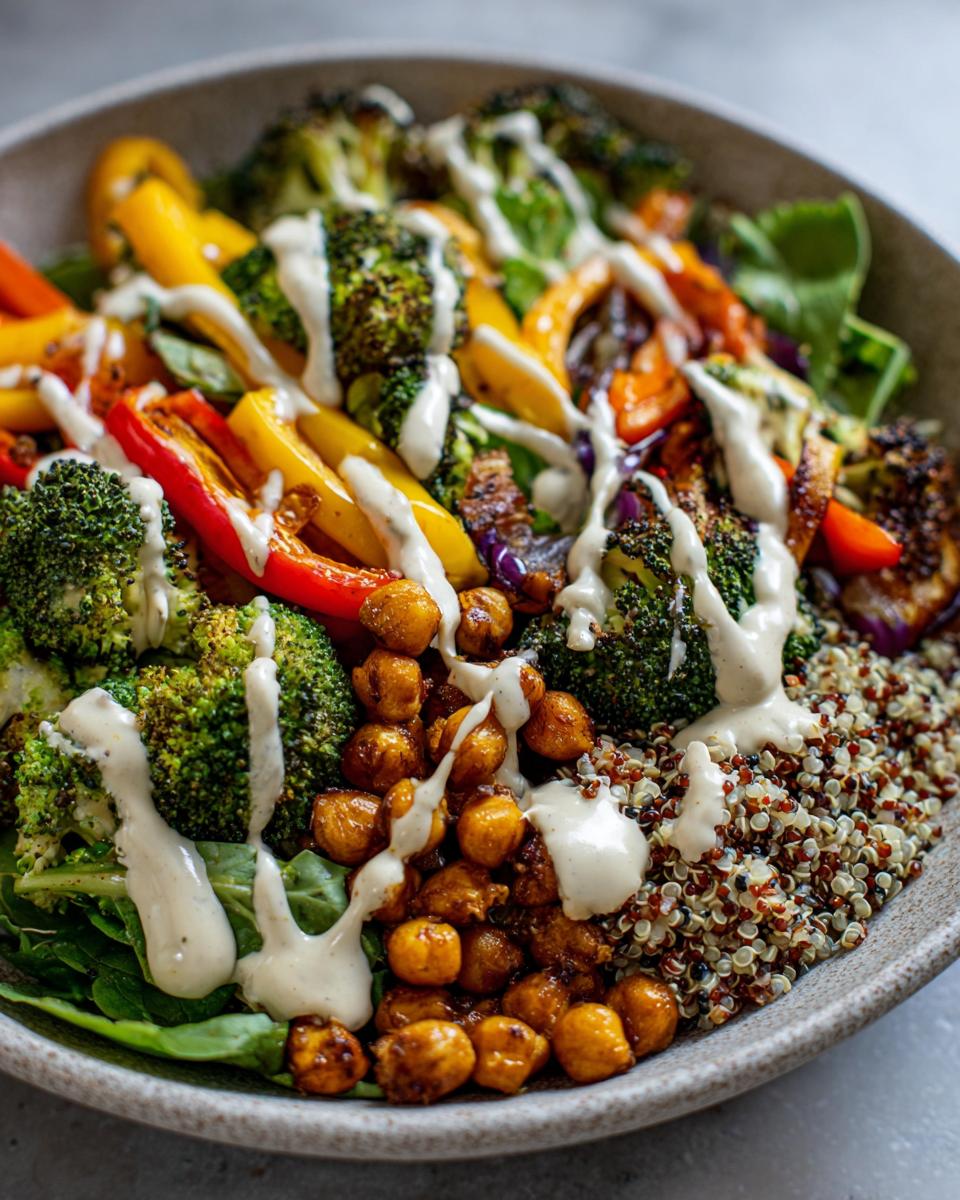 A vibrant Buddha bowl filled with roasted broccoli, bell peppers, chickpeas, quinoa, and drizzled with a creamy dressing.