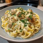 A close-up of creamy Chicken Alfredo pasta with fettuccine, topped with golden-brown meatballs and fresh parsley.