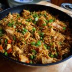 Close-up of a skillet filled with delicious chicken fried rice, featuring tender chicken pieces, peas, carrots, and green onions.
