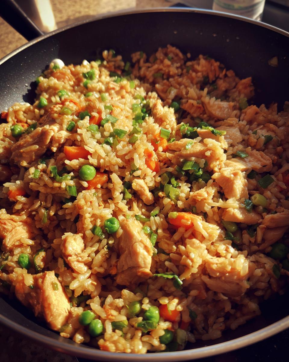 Close-up of freshly made chicken fried rice with peas, carrots, and green onions in a skillet.
