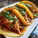 Close-up of three flavorful chicken tacos filled with shredded chicken, topped with cilantro and cheese.