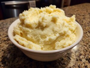 A close-up of a white bowl filled with creamy, fluffy mashed potatoes.