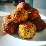 A stack of perfectly golden-brown, crispy falafel balls with visible herbs.