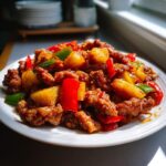 A plate of crispy sweet and sour pork with chunks of pineapple, red and green bell peppers.