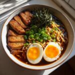 A close-up of a delicious ramen bowl featuring tender pork slices, a perfectly cooked soft-boiled egg, and green onions.