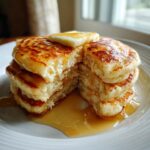 A stack of fluffy pancakes topped with butter and dripping with syrup.