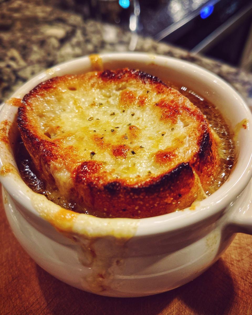 Close-up of a bubbling bowl of French onion soup, topped with a thick layer of melted, golden-brown cheese and toasted bread.