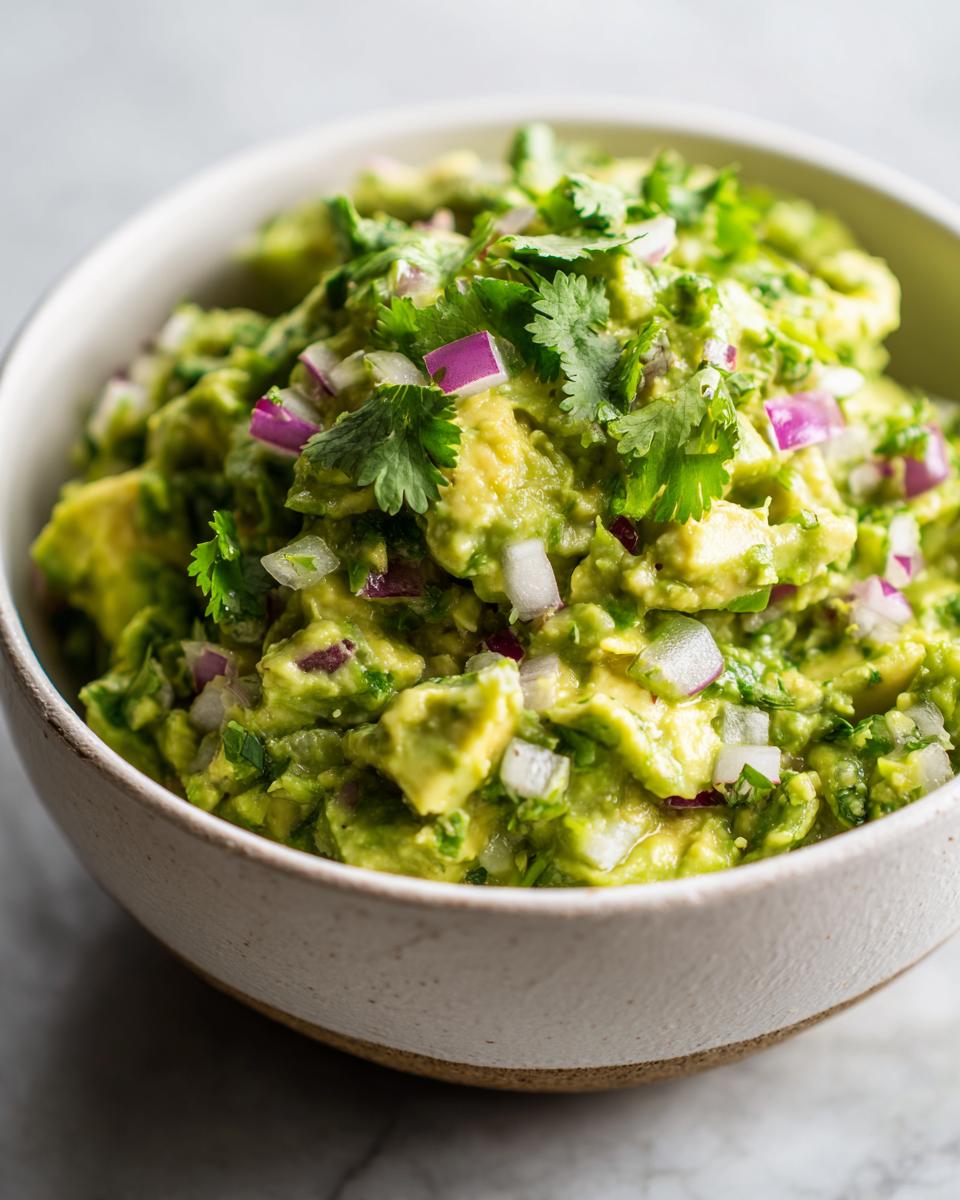 A close-up of a bowl of chunky Guacamole, topped with fresh cilantro and diced red onion.