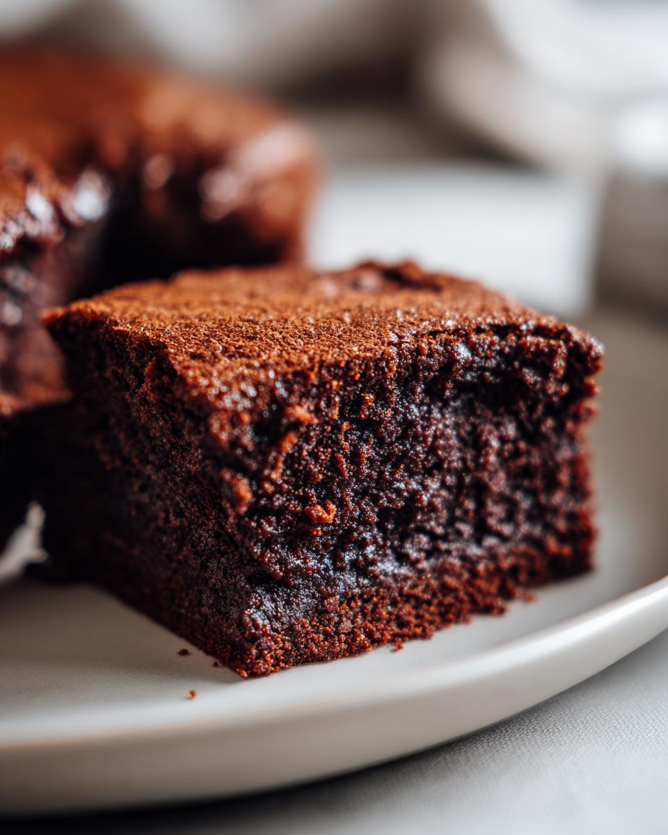 Close-up of a rich, dark chocolate fudge brownie dusted with cocoa powder on a plate.