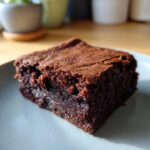 A close-up of a rich, fudgy brownie with a cracked top, ready to be enjoyed.