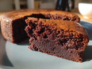 A close-up of a rich, dark chocolate fudge brownie slice on a grey plate, showcasing its moist texture.