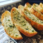 Close-up of golden-brown slices of homemade garlic bread, sprinkled with chopped parsley.