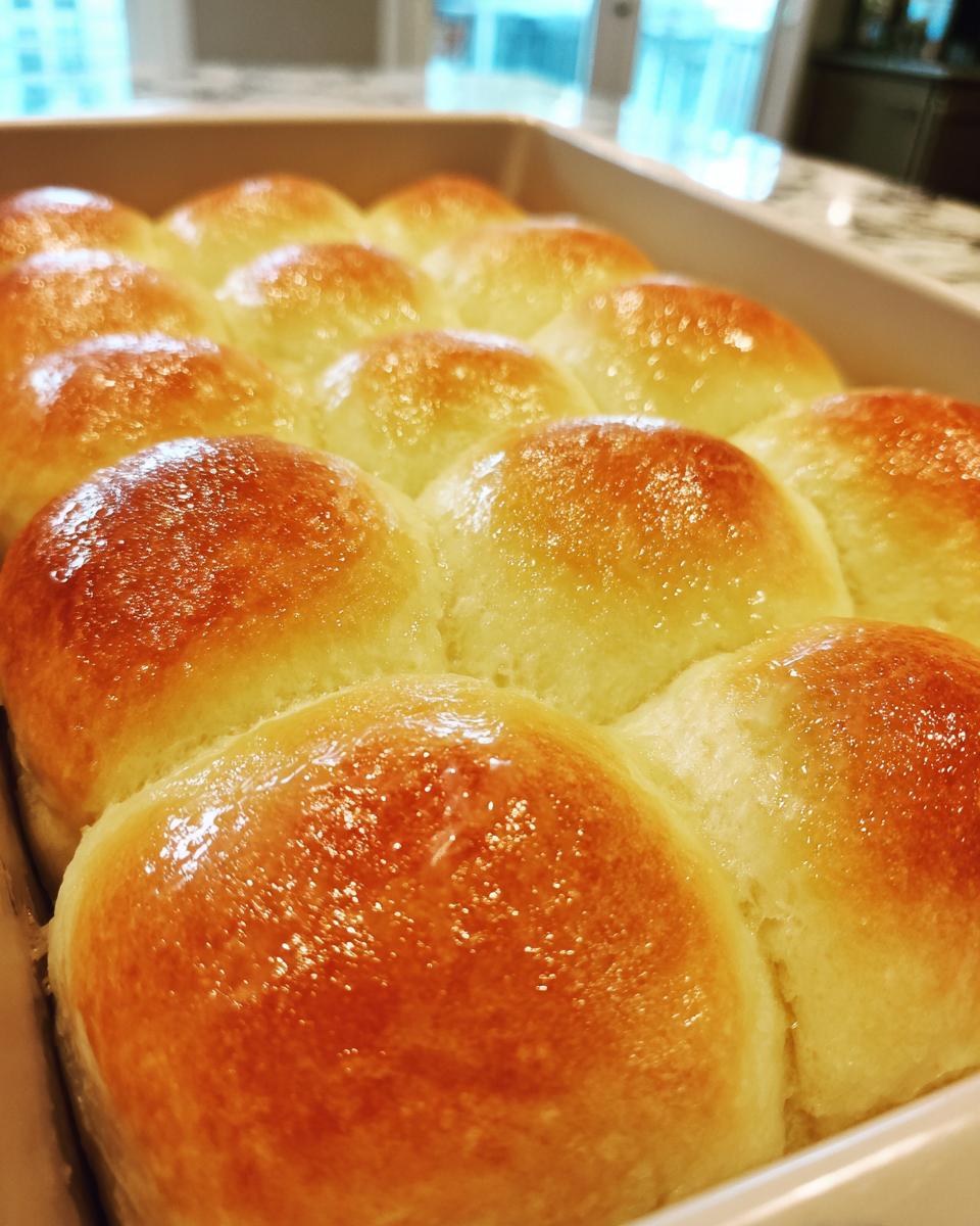 Close-up of a pan of golden brown, freshly baked dinner rolls with a glossy sheen.