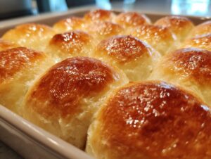 Close-up of golden brown, fluffy dinner rolls baked in a white dish, ready to serve.