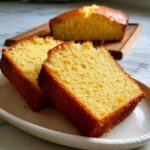Two slices of golden-brown Grandma's Perfect Pound Cake on a white plate, with a whole loaf in the background.