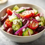 Close-up of a vibrant Greek salad in a bowl, featuring fresh tomatoes, cucumbers, red onions, Kalamata olives, and feta cheese.