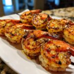 Close-up of perfectly grilled shrimp skewers seasoned with herbs and spices, served on a white plate.